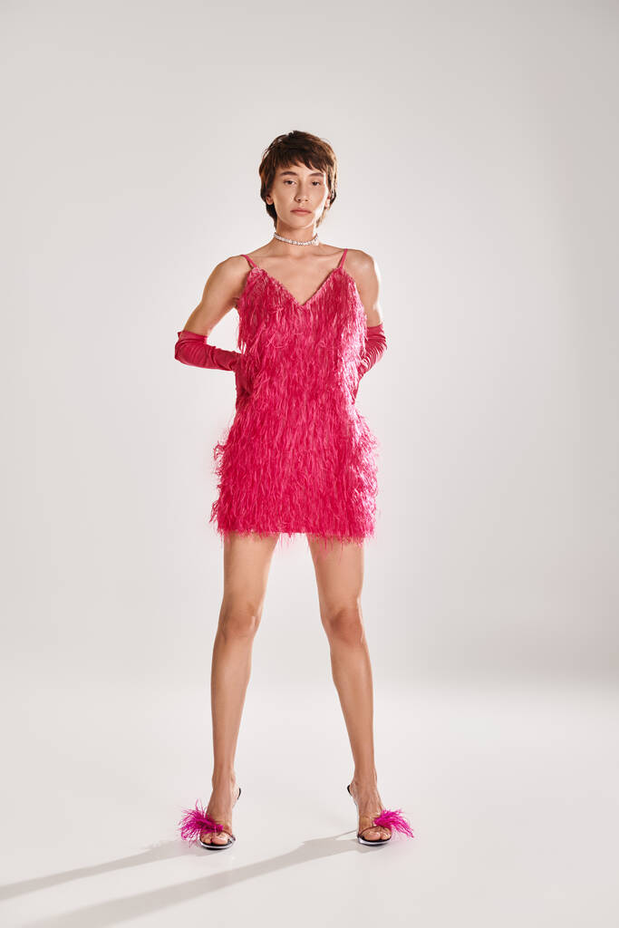 A fashionable young woman poses in an elegant pink feather dress against a vibrant backdrop. - Photo, Image