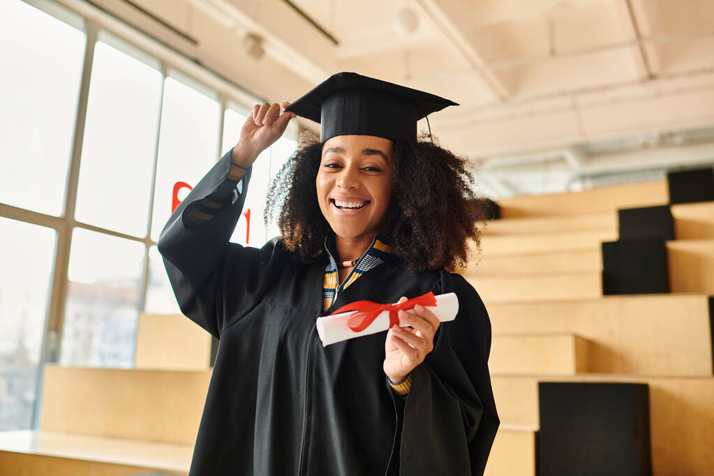 Una mujer afroamericana se enorgullece de llevar un gorro de graduación y un vestido, celebrando sus logros académicos.. - Foto, imagen