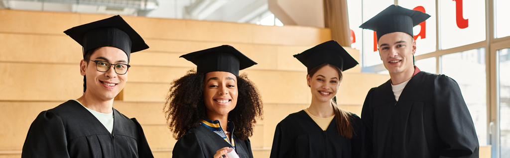 Мультикультурная группа студентов в выпускных шапках и платьях празднует академический успех в помещении. - Фото, изображение