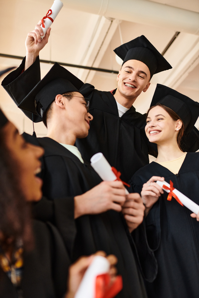 Un grupo diverso de estudiantes se une en vestidos de graduación y gorras académicas, unidos en celebración y felicidad. - Foto, imagen