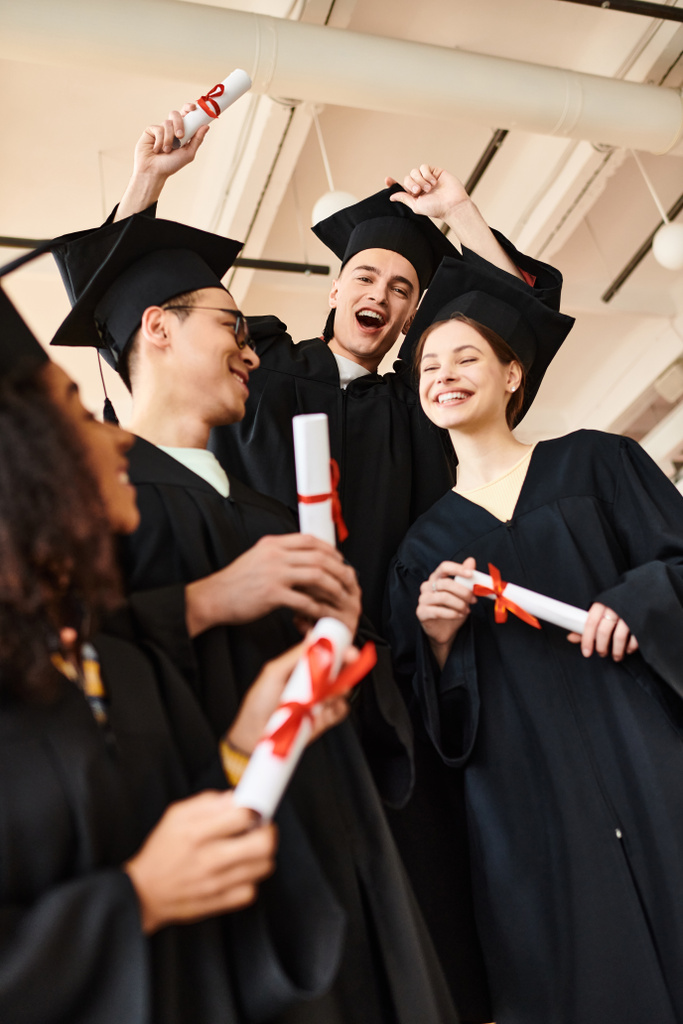 Un gruppo di studenti diversi in abiti da laurea e berretti stare insieme, celebrando i loro risultati accademici. - Foto, immagini