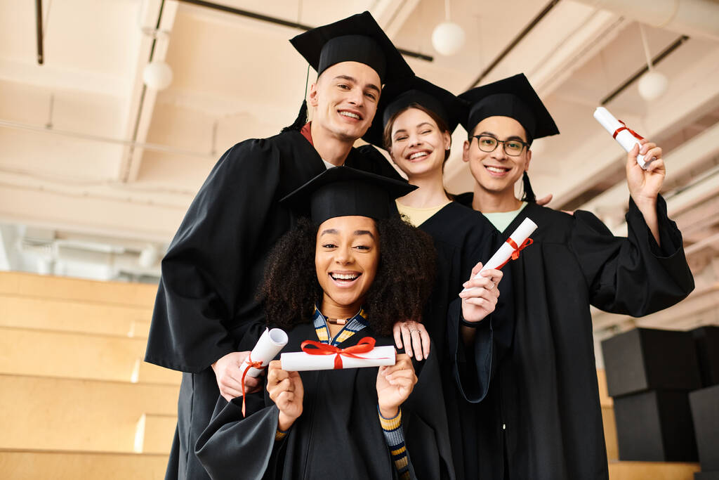 Divers groupes d'étudiants en robes de remise des diplômes et casquettes académiques souriant joyeusement pour une photo à l'intérieur. - Photo, image