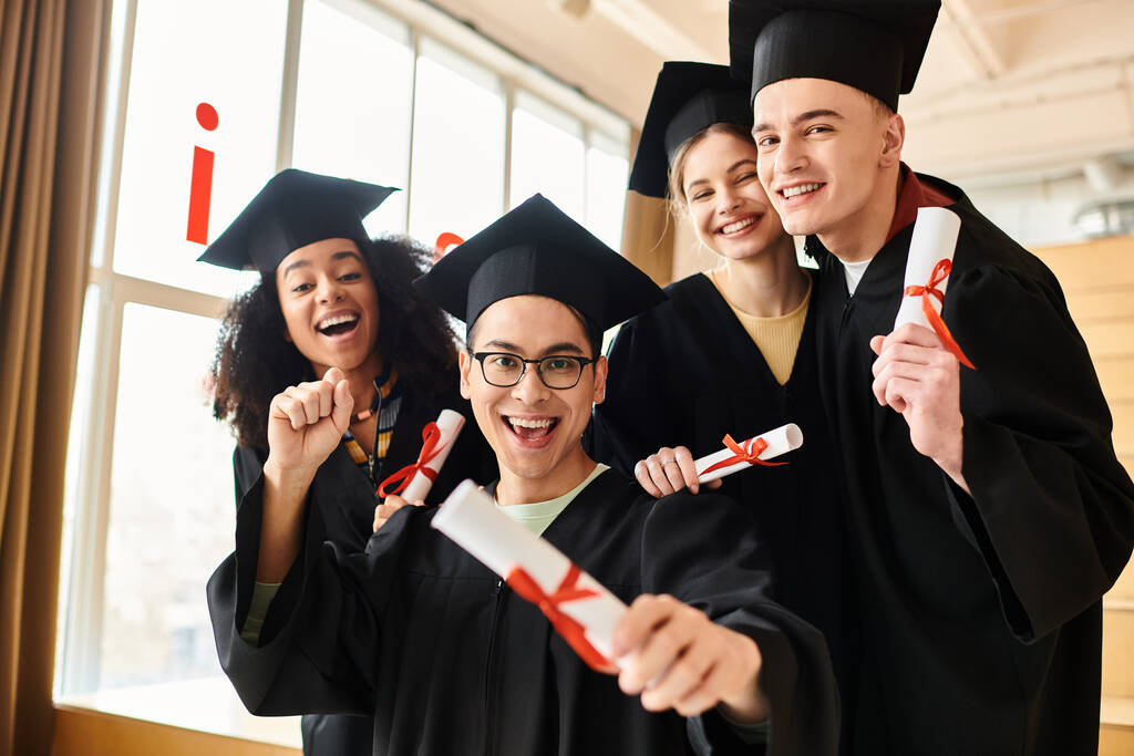 Un grupo diverso de estudiantes en trajes de graduación y gorras posando alegremente para una foto para conmemorar su éxito académico. - Foto, Imagen