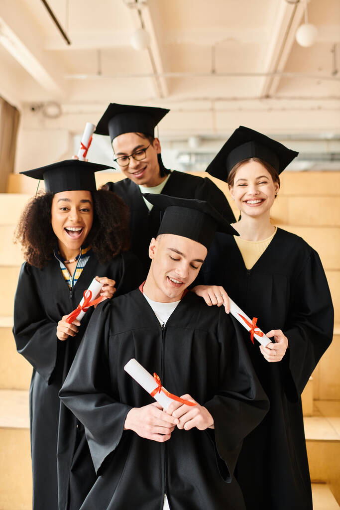 Diverso gruppo di studenti in abiti di laurea e tappi accademici in posa felicemente per una foto al chiuso. - Foto, immagini