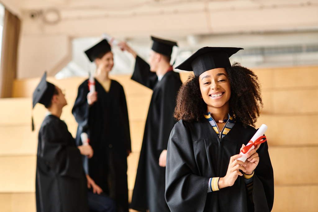 Zróżnicowana kobieta dumnie stoi w czapce i sukni dyplomowej, trzymając dyplom. - Zdjęcie, obraz