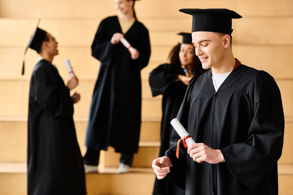 Ein vielseitiger Mann im Abschlusskleid hält stolz sein Diplom in der Hand. - Foto, Bild