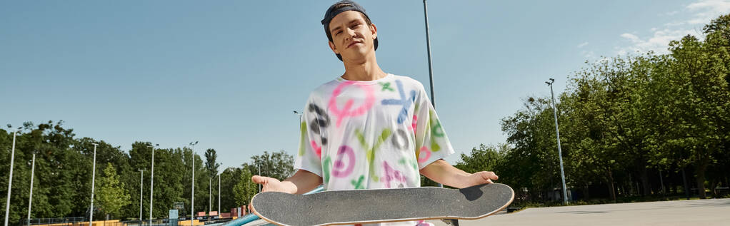 Un jeune homme élégant tient son skateboard dans un parking, prêt à descendre dans la rue avec son prochain tour. - Photo, image