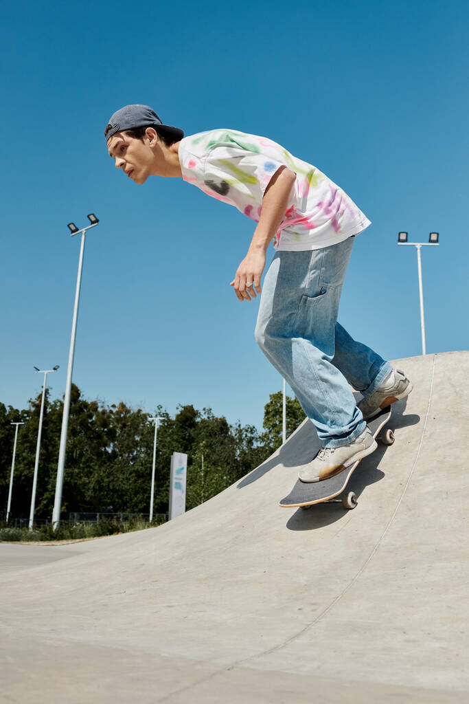 Młody człowiek bez wysiłku ślizga się po rampie na deskorolce w tętniącym życiem skateparku w słoneczny letni dzień. - Zdjęcie, obraz