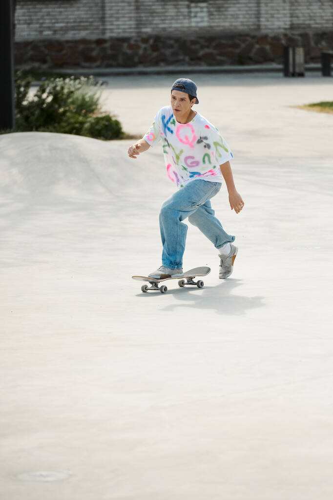Un joven skater monta con confianza en su monopatín por una rampa de cemento en un parque de skate en un día soleado de verano.. - Foto, imagen