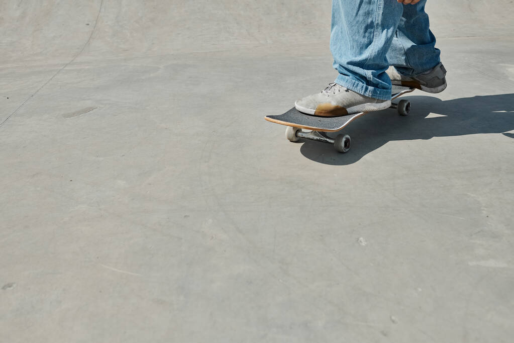 Молодой скейтбордист без особых усилий катается на скейтборде по гладкой цементной поверхности в ярком открытом скейтпарке в летний день. - Фото, изображение
