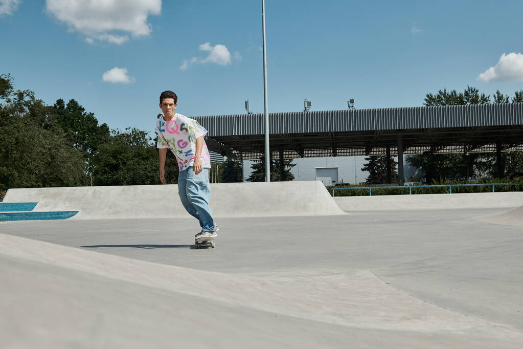 A daring young skater boy fearlessly rides his skateboard down the side of a ramp in a sunny outdoor skate park. - Photo, Image