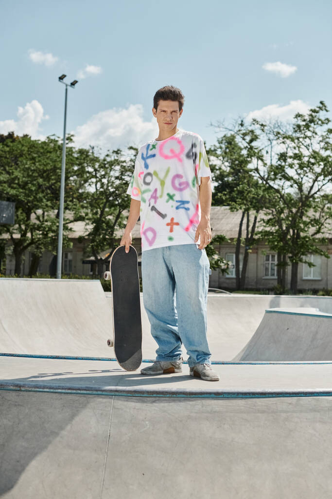 Молодой человек наслаждается летним днем в ярком скейт-парке, держа скейтборд и готовый к поездке. - Фото, изображение