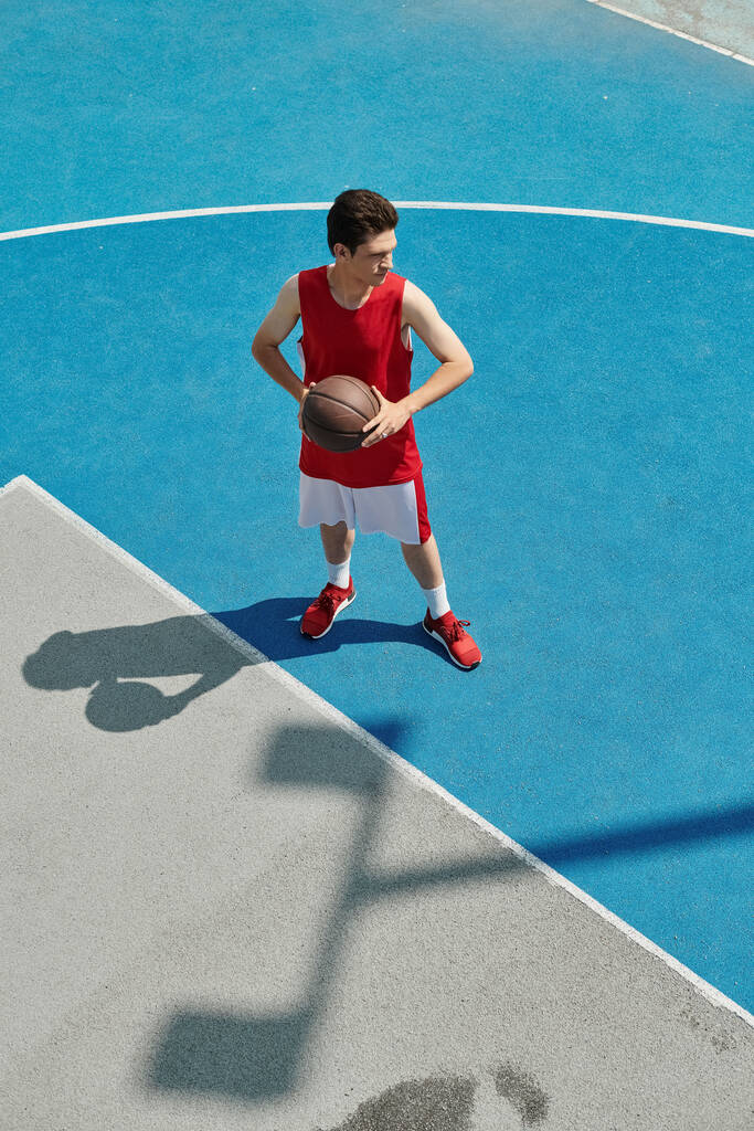 Un giovane di talento tiene fiducioso un pallone da basket mentre è in piedi su un campo, affinando le sue abilità - Foto, immagini