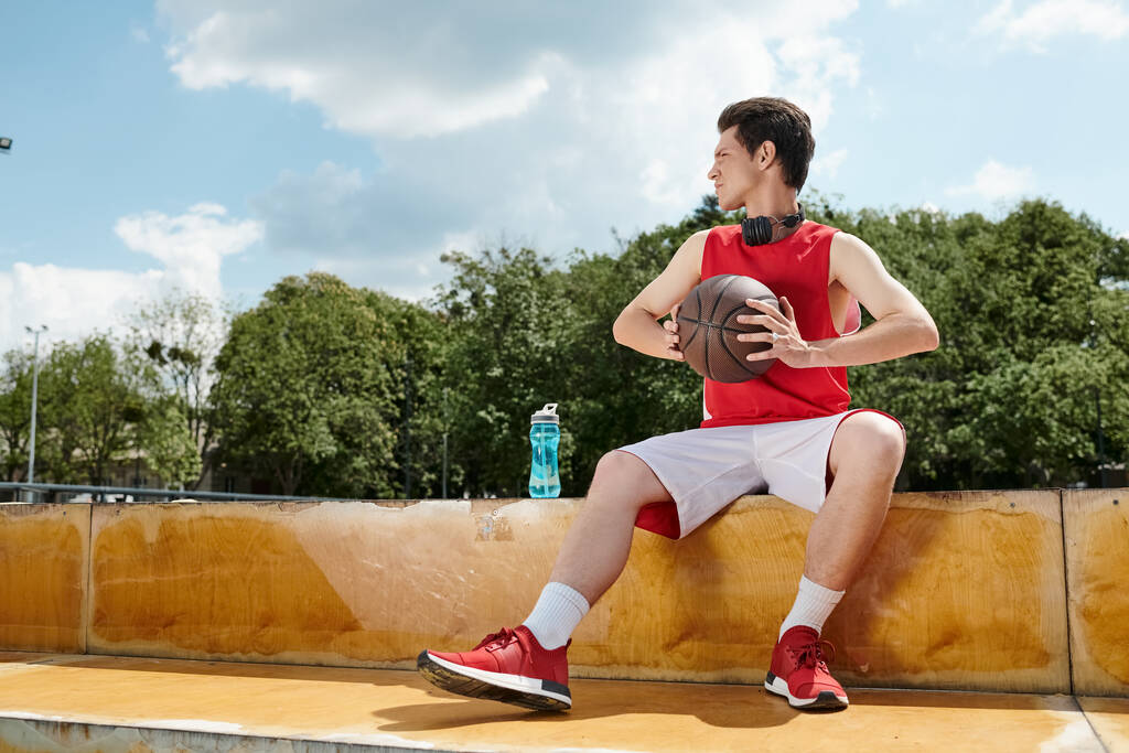 Młody koszykarz siedzący na parapecie, umiejętnie trzymający koszykówkę. - Zdjęcie, obraz
