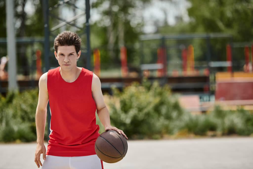 Un jeune homme dans une chemise rouge vibrante montre ses compétences de basket en plein air par une journée d'été ensoleillée. - Photo, image