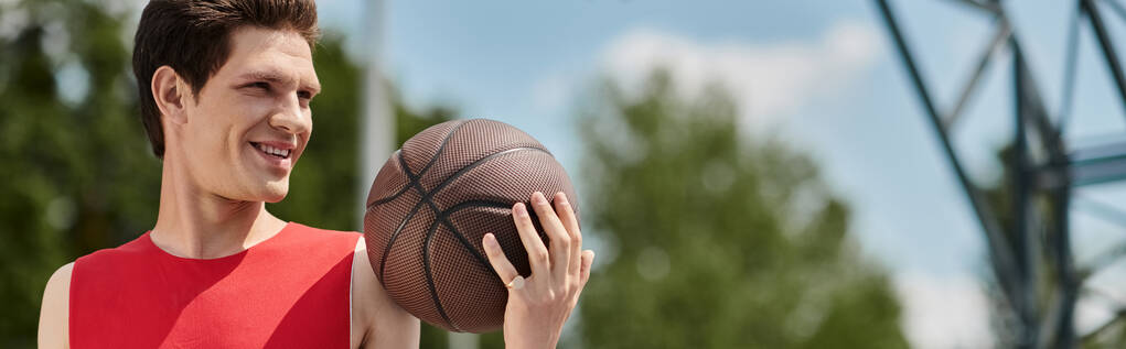 Un giovane uomo con una camicia rossa sapientemente dribbling una pallacanestro all'aperto in una calda giornata estiva. - Foto, immagini