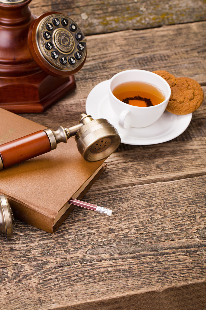 Elfenbein-Teetasse mit süßem Keks, altem Telefon und Buch auf Holz - Foto, Bild