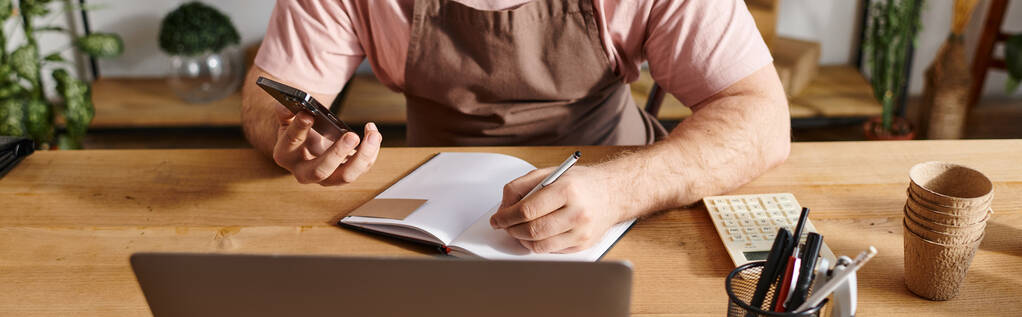 Un hombre inmerso en el trabajo, sentado en un escritorio con un cuaderno y un teléfono celular, centrado en sus ideas de pequeña empresa. - Foto, imagen