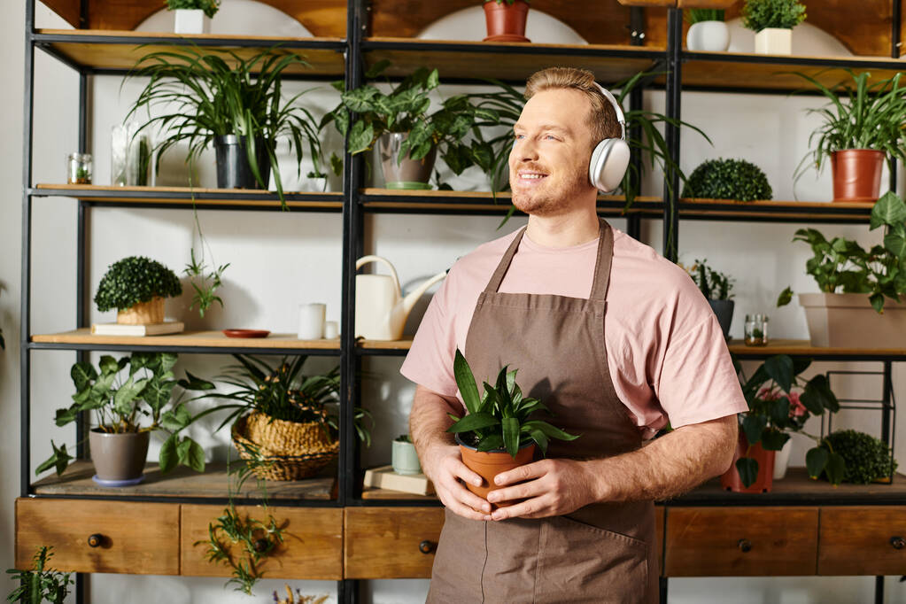 Ein Mann mit Kopfhörern balanciert eine Topfpflanze, versinkt in Musik und pflegt sein Grün. - Foto, Bild
