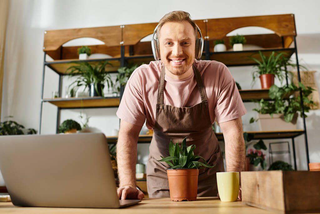 Een man met een koptelefoon zit voor een laptop, ondergedompeld in zijn werk, in een plantenwinkel. Hij straalt focus en creativiteit uit. - Foto, afbeelding
