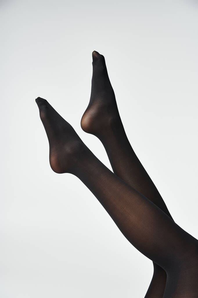 Молодая женщина демонстрирует свои ноги в черных чулках на сером фоне студии. - Фото, изображение