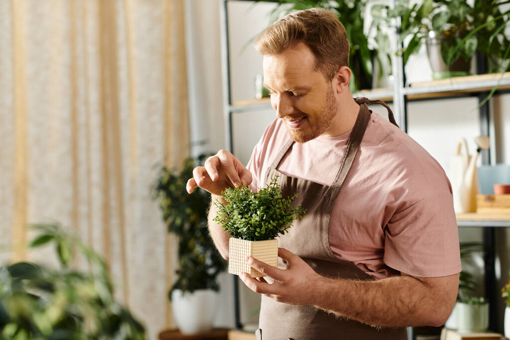 Un homme dans un tablier tient doucement une plante en pot, dépeignant soins et tendresse dans un cadre d'atelier de plantes. - Photo, image