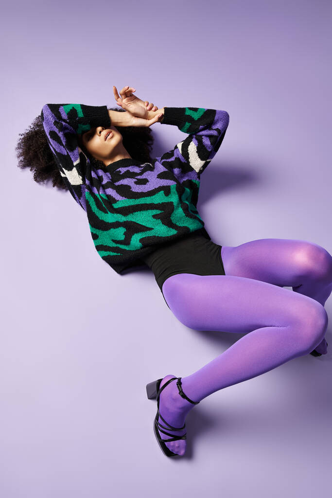 スタジオの設定で紫色の地面に優雅に横たわる活気のあるタイツとセーターの若い女性. - 写真・画像