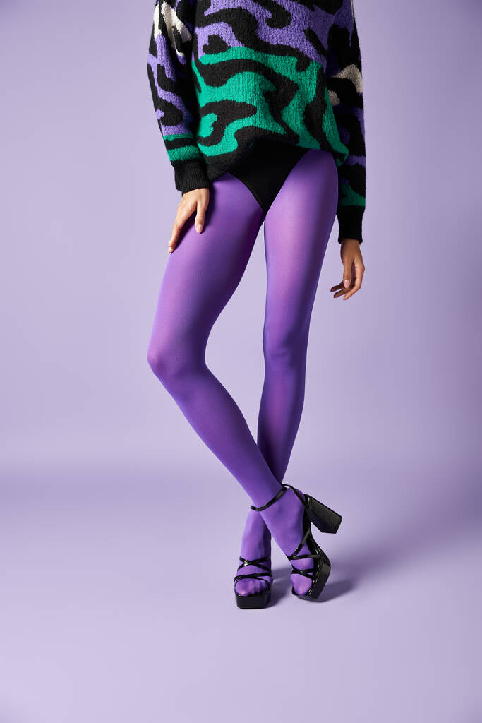 Mladá žena oblečená v pulzujících fialových punčocháčích a svetru, které zaujímají pózu ve studiu na purpurovém pozadí. - Fotografie, Obrázek