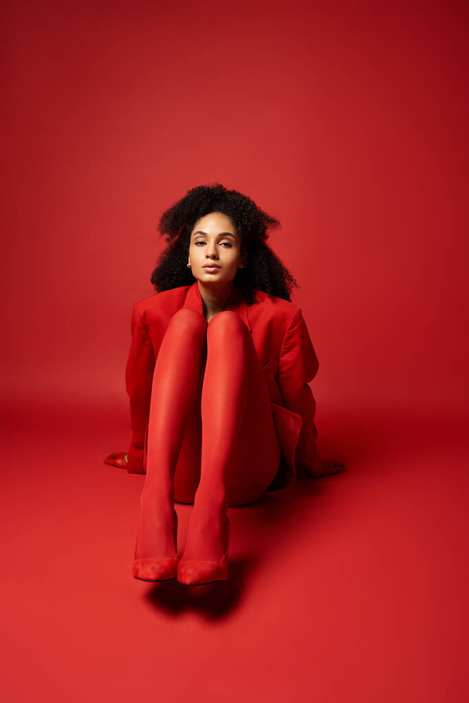 Una mujer joven con una chaqueta roja y medias se sienta en el suelo en un ambiente vibrante estudio. - Foto, Imagen