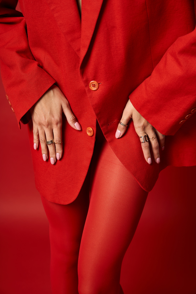Eine stylische junge Frau steht selbstbewusst in rotem Anzug und passenden Strümpfen vor lebendigem Studiohintergrund. - Foto, Bild