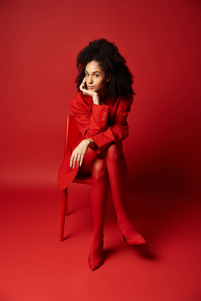 Egy elegáns, fiatal nő élénk piros ruhában, kecsesen ül egy megfelelő széken.. - Fotó, kép