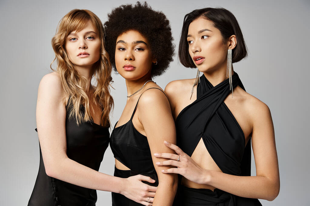 Siyah elbiseli üç farklı kadın, gri bir stüdyonun arka planında zarif bir şekilde yan yana duruyorlar.. - Fotoğraf, Görsel