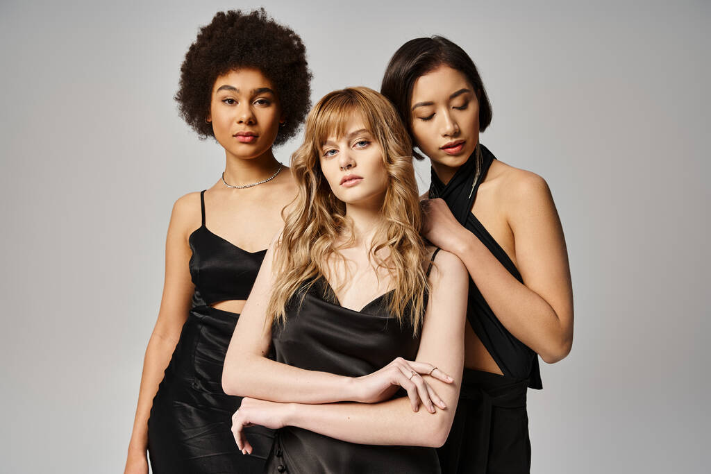 Tři elegantní ženy různých ras stojí půvabně spolu na šedém pozadí. - Fotografie, Obrázek