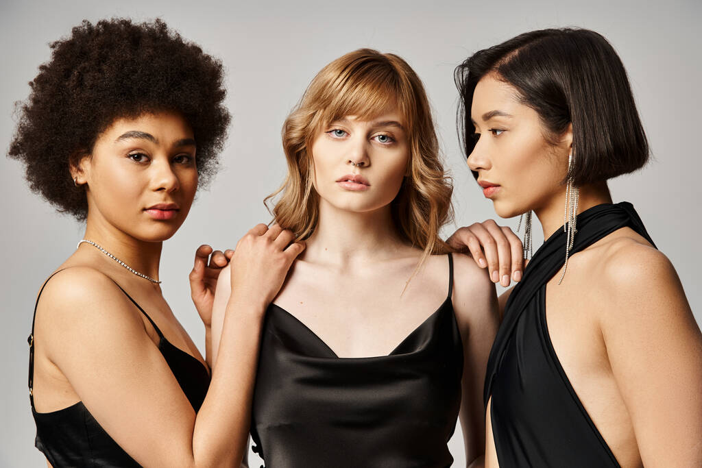Drie mooie vrouwen van blanke, Aziatische en Afro-Amerikaanse afkomst staan elegant op een grijze studio-achtergrond. - Foto, afbeelding