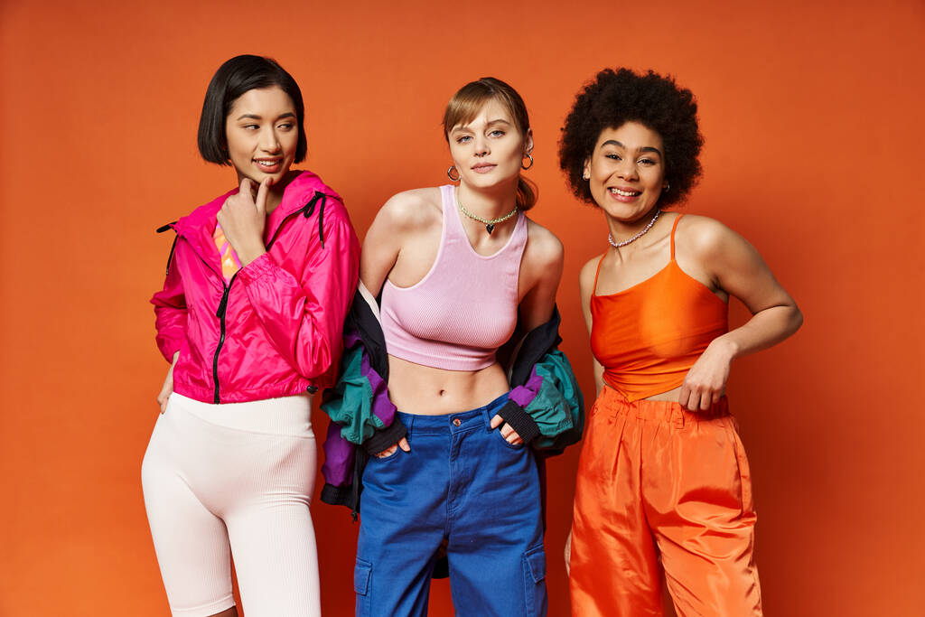 活気に満ちたオレンジ色の背景に多様性と団結を表す,異なる民族の3人の女性. - 写真・画像