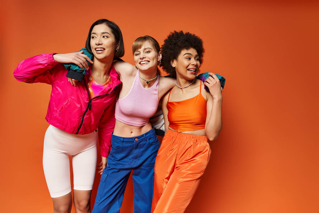 白人,アジア人,アフリカ系アメリカ人を含む多様な女性グループが,活気に満ちたオレンジ色の背景と共に立っています.. - 写真・画像