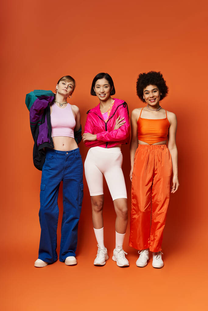 Biała, Azjatka i Afroamerykanka stojąca razem przed pomarańczowym studiem. - Zdjęcie, obraz