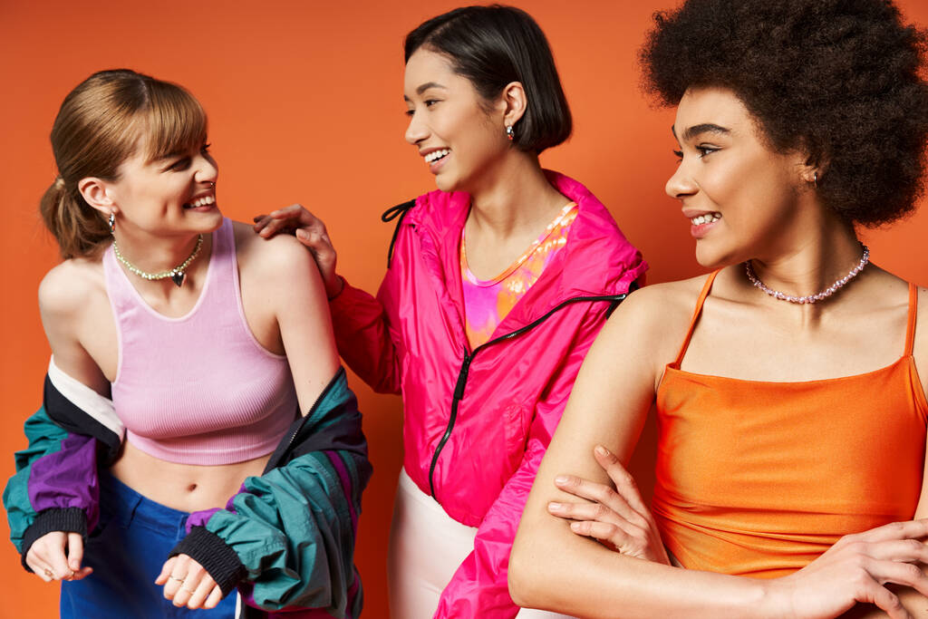 A diverse group of women of different ethnic backgrounds standing together, exuding strength and unity on an orange studio background. - Photo, Image