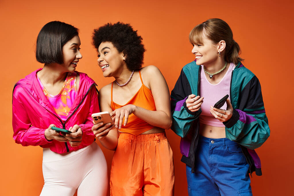 Tres mujeres de diversas etnias de pie juntas, mirando atentamente la pantalla de un teléfono celular. - Foto, Imagen