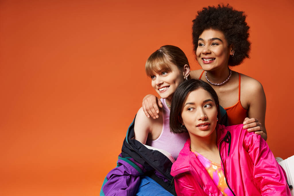Deux femmes de races différentes posent avec amour avec un enfant heureux devant un fond de studio orange. - Photo, image
