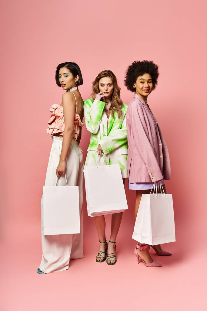 Τρεις γυναίκες διαφορετικών εθνικοτήτων που κρατούν τσάντες για ψώνια σε ροζ φόντο. - Φωτογραφία, εικόνα