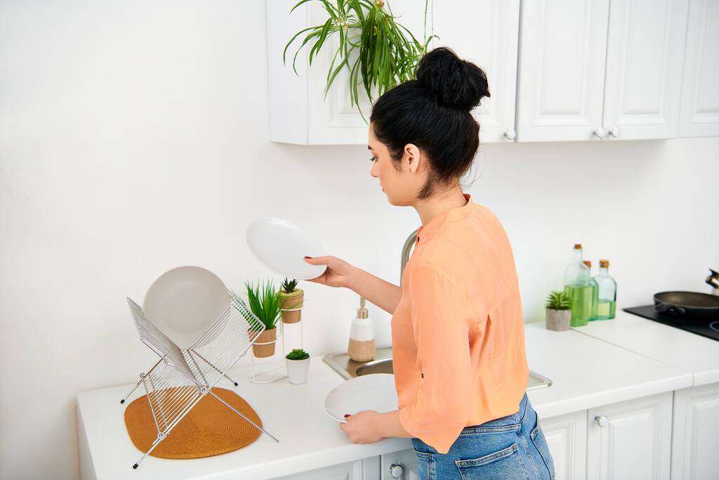 Una mujer elegante con atuendo casual de pie en un mostrador de cocina, sosteniendo un frisbee blanco. - Foto, imagen