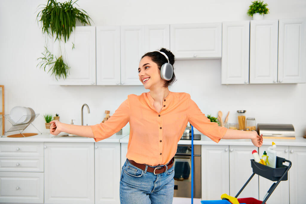Een stijlvolle vrouw met een koptelefoon staat in een keuken. - Foto, afbeelding