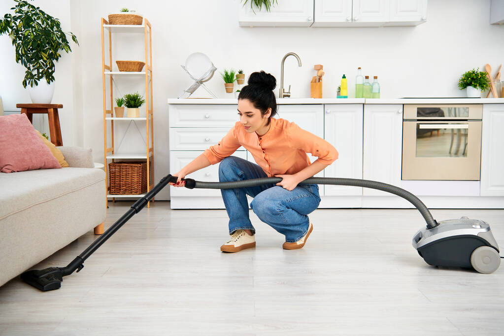 A stylish woman in casual attire gracefully vacuums the floor with her sleek vacuum cleaner, bringing cleanliness to her home. - Photo, Image