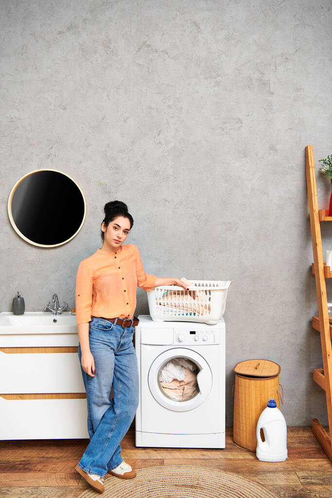 Uma mulher casualmente vestida ao lado de uma máquina de lavar roupa, cuidando de suas tarefas domésticas. - Foto, Imagem