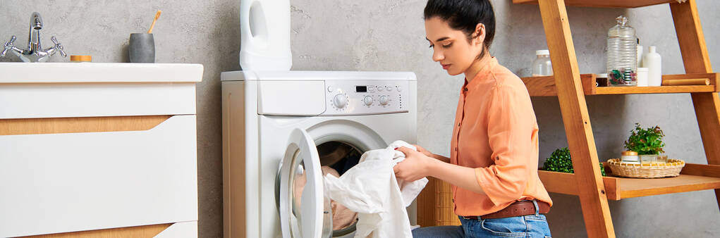 A stylish woman in casual clothing gracefully places a cloth into a humming dryer. - Photo, Image