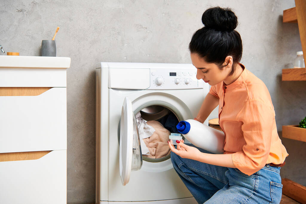 Stylowa kobieta wlewa wodę do pralki w jej modnym domu do czyszczenia ubrań. - Zdjęcie, obraz