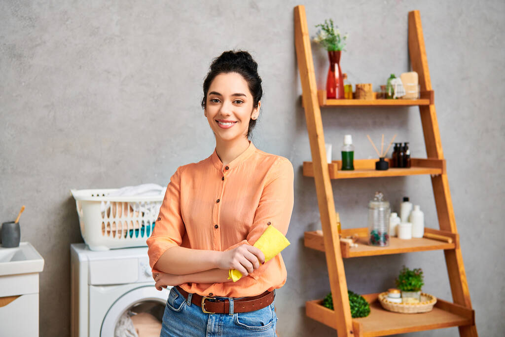 Стильна жінка в повсякденному вбранні стоїть поруч з пральною машинкою у ванній кімнаті, орієнтована на прання. - Фото, зображення