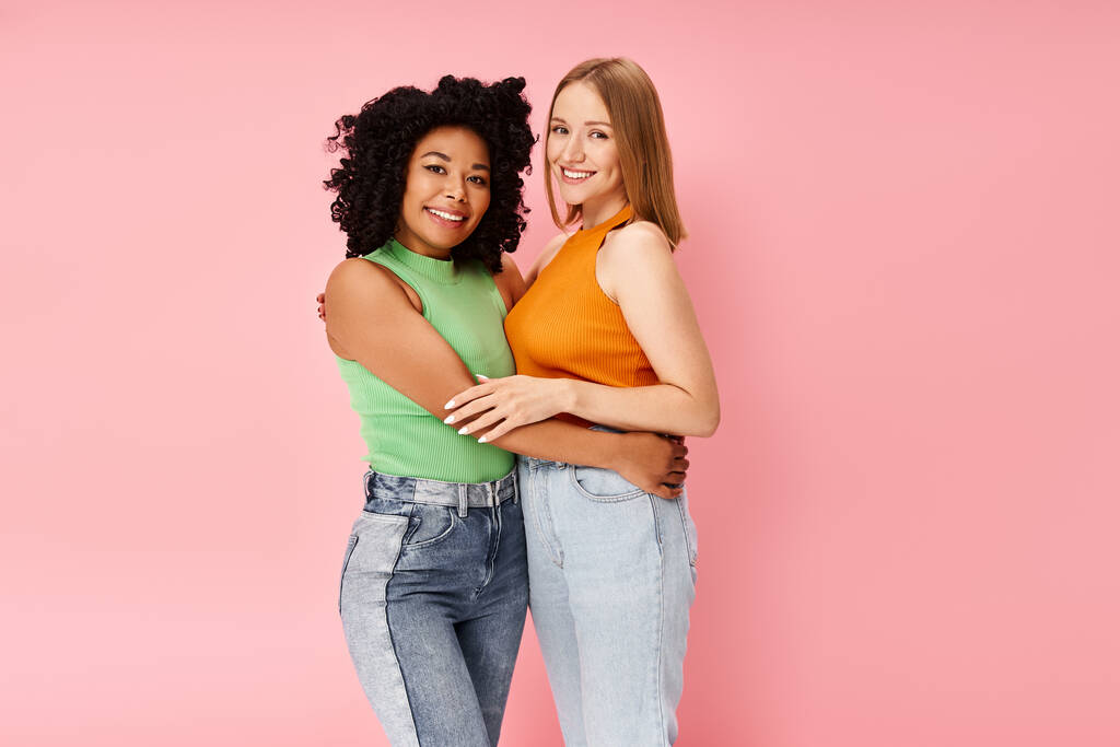 Dos mujeres atractivas y diversas en un atuendo acogedor comparten un abrazo sincero frente a un telón de fondo rosa. - Foto, Imagen