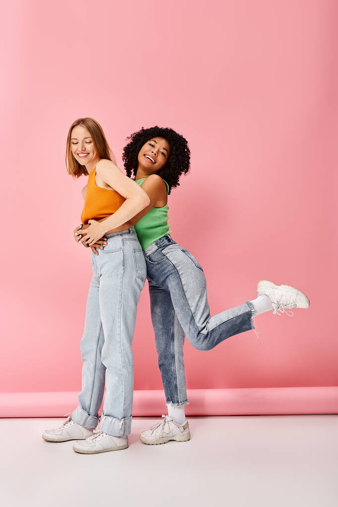 Dos mujeres jóvenes con atuendo casual se abrazan frente a una pared rosa. - Foto, Imagen